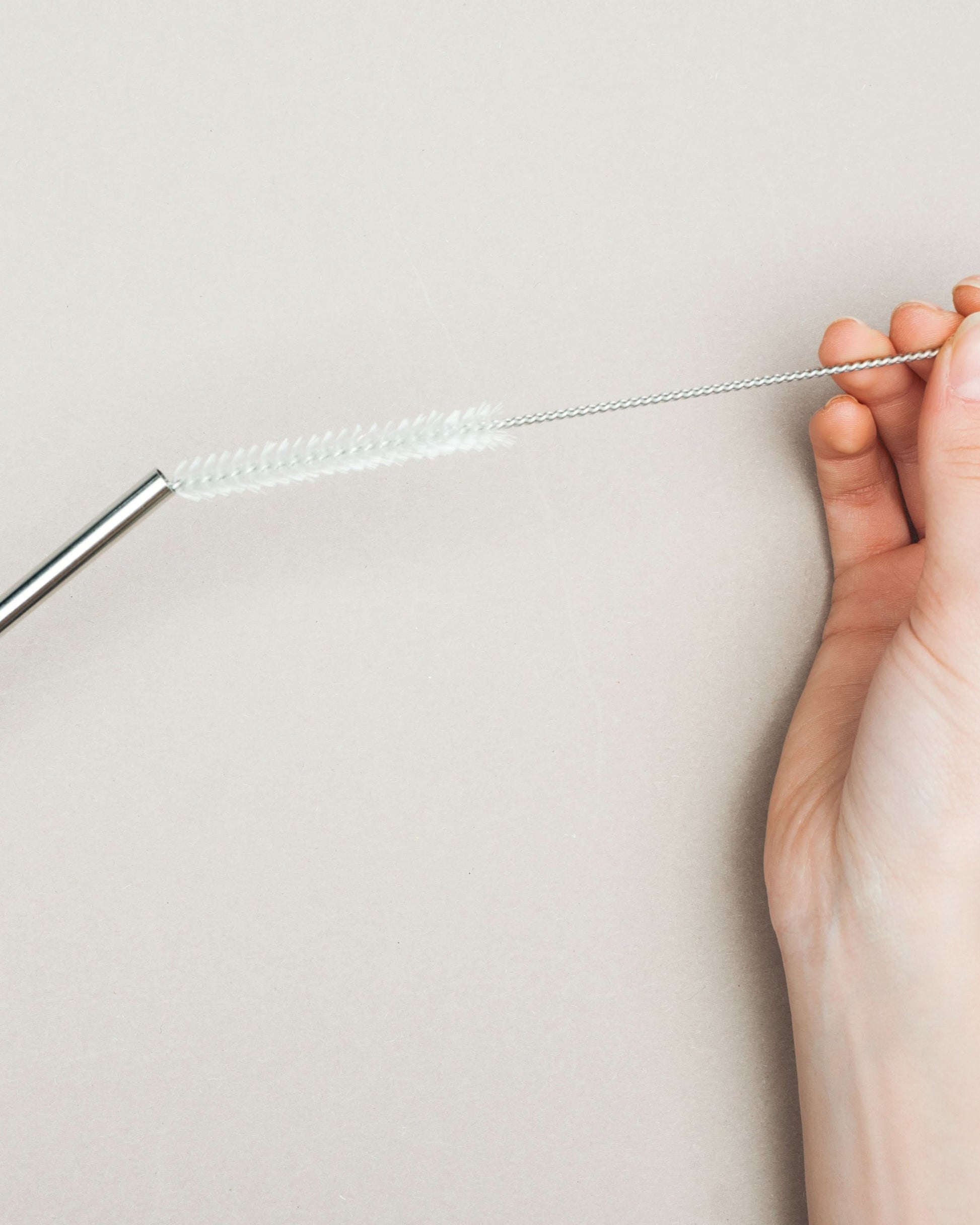 Hand holding a straw cleaning brush inserted into a stainless steel straw, demonstrating proper use for thorough cleaning.